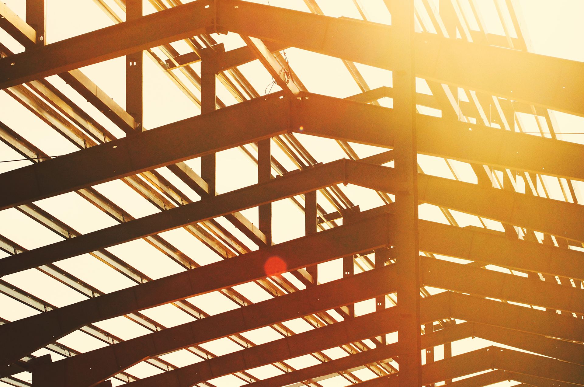 Structural steel framing of a building under construction, backlit at sunset